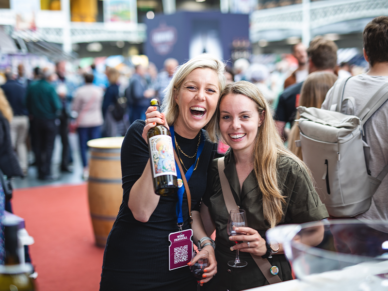 Two women joyfully holding a bottle of wine, celebrating together in a warm and inviting atmosphere.