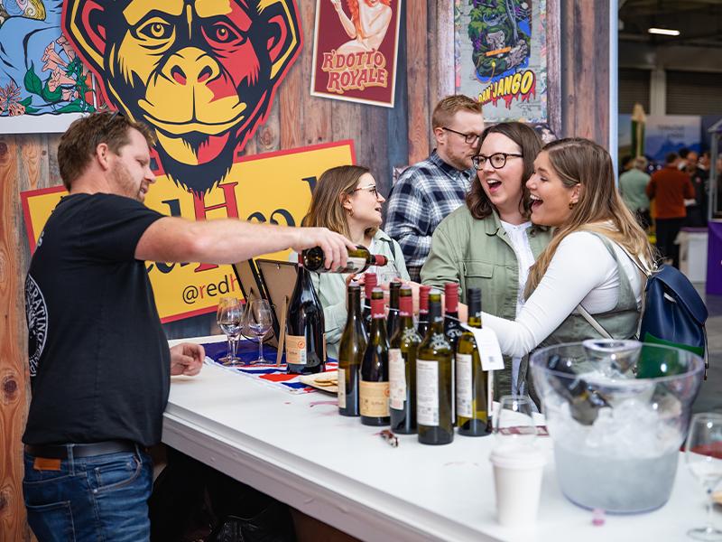 People socializing around a table adorned with wine bottles.