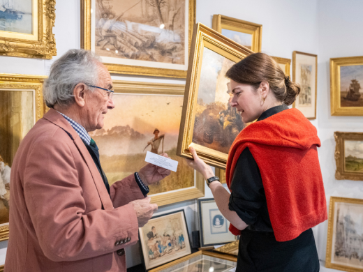 A woman holding an artwork, engaged in conversation with an elder gentlemen.