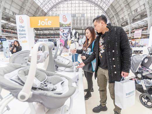 A man and woman examine various baby products together at a lively event.