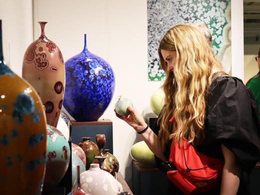 A woman gazes thoughtfully at a decorative vase, contemplating its design and beauty.