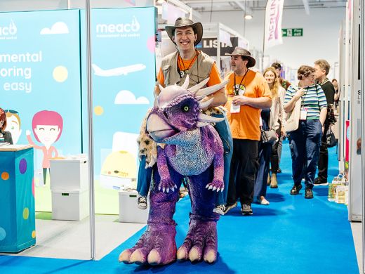 A man dressed in dinosaur costume at a trade event.