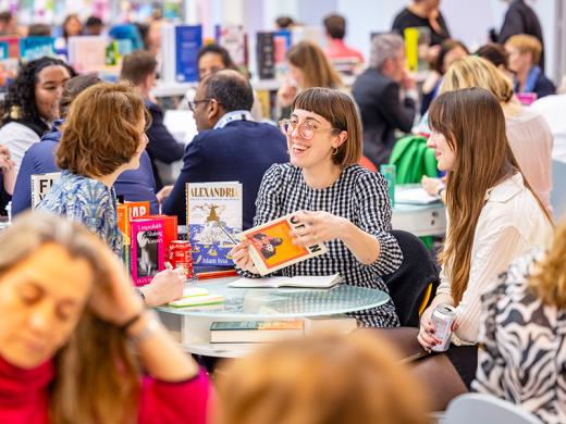 A diverse group of individuals engaged in reading and discussion at tables filled with books in a cozy setting.