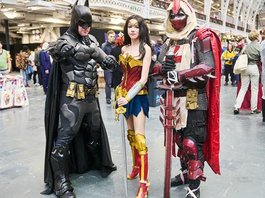 Three individuals dressed as Batman, Wonder Woman, and Superman, showcasing iconic superhero costumes in a vibrant setting.