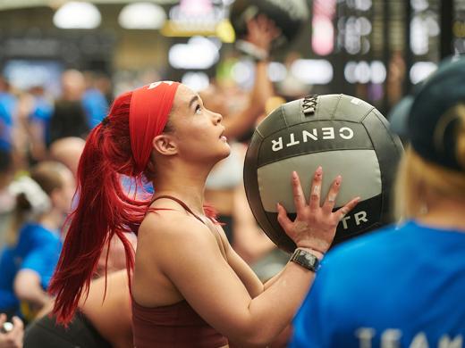 A woman with vibrant red hair is holding a medicine ball, showcasing strength and determination in her posture.