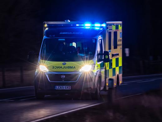 An ambulance with a blue light driving in the dark.