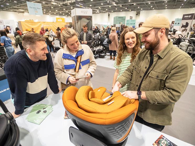 Visitors inspecting baby car seat at exhibition.