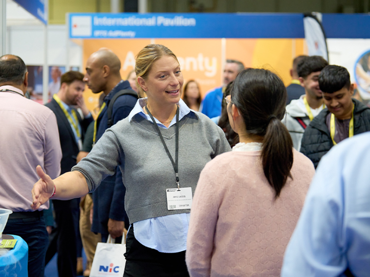 Two individuals in conversation at a bustling trade show.