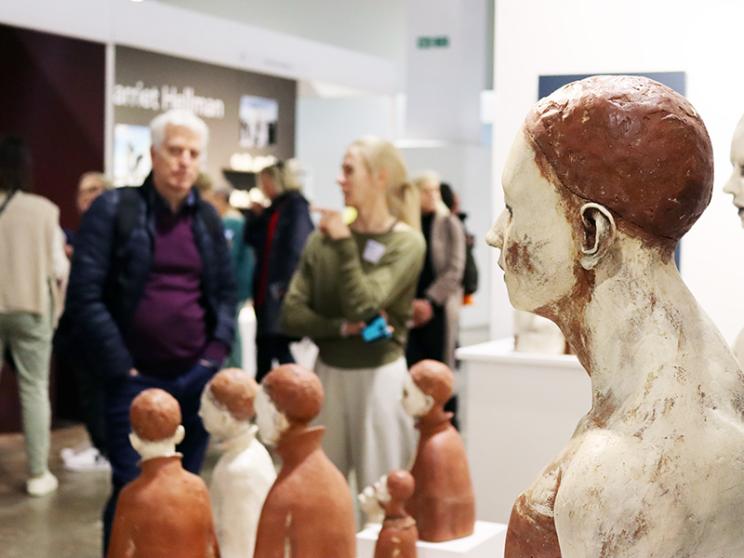 A diverse group of individuals admiring a collection of intricate sculptures in a gallery setting.
