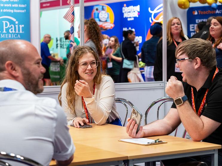 Three individuals engaged in conversation while seated at a table, sharing ideas and thoughts in a friendly setting.