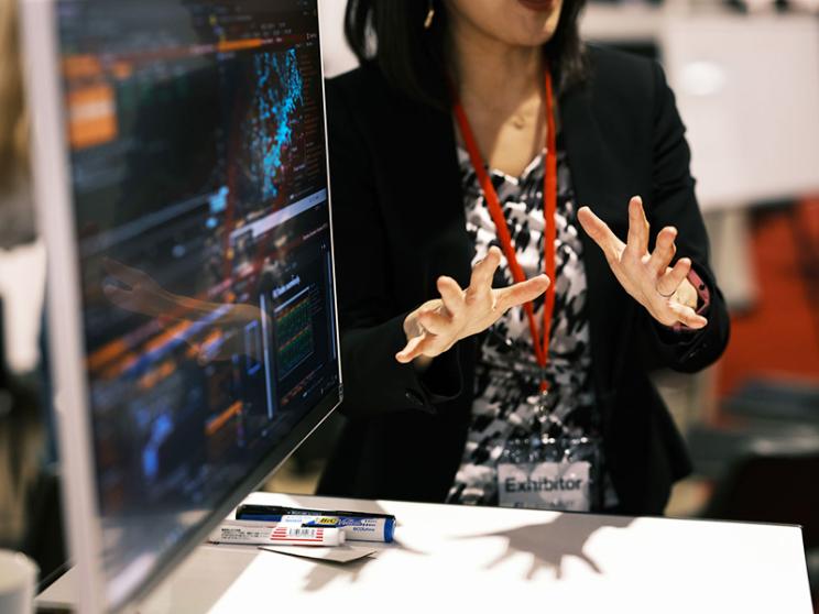 A woman is pointing at a computer screen, indicating something of interest or importance displayed on it.