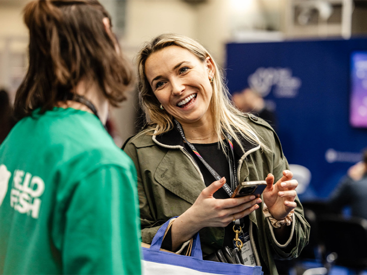 A woman smiles warmly at another individual at an event.