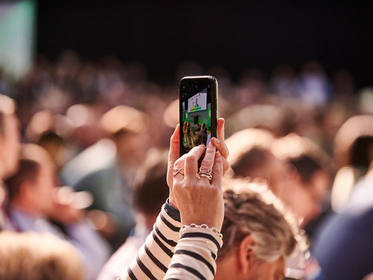 Person holding up a smartphone to record a crowded event, capturing the stage on the screen.