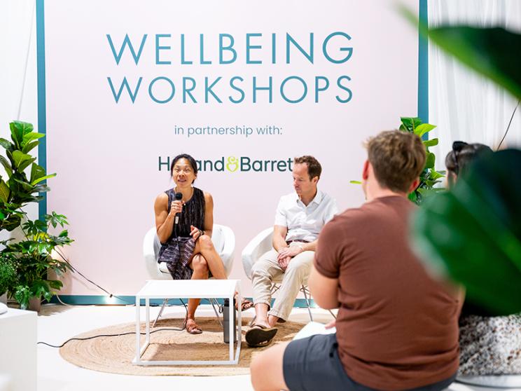 A diverse group of individuals seated in chairs, gathered in front of a sign promoting wellness workshops.