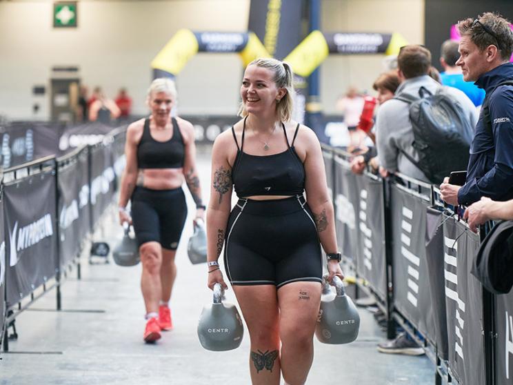 A woman athlete smiling whilst holding weights.