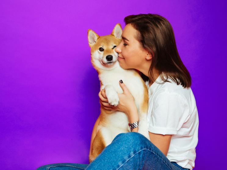 A girl holding a dog against a purple background