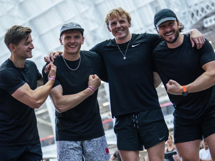 First Image: A group of four men wearing black athletic clothing pose together, smiling and flexing their arms in a friendly, celebratory manner. 