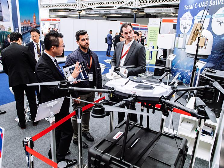 Attendees at a trade show discussing products at a booth featuring unmanned aerial vehicles (UAVs).