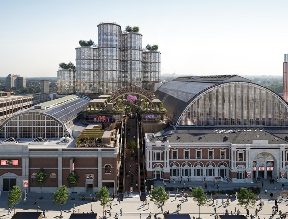 Aerial view of Olympia London showing the iconic arched exhibition halls alongside new glass tower structures and rooftop gardens, illustrating the site's transformation into a modern cultural destination.