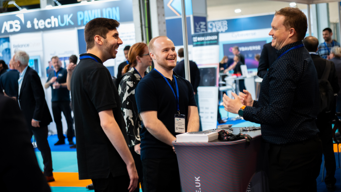 Three men engaged in conversation at a trade show.