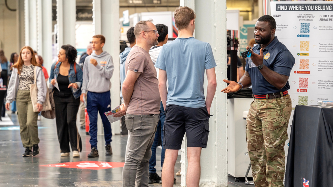 Father and son talking to a man wearing army pants at an exhibition stand.