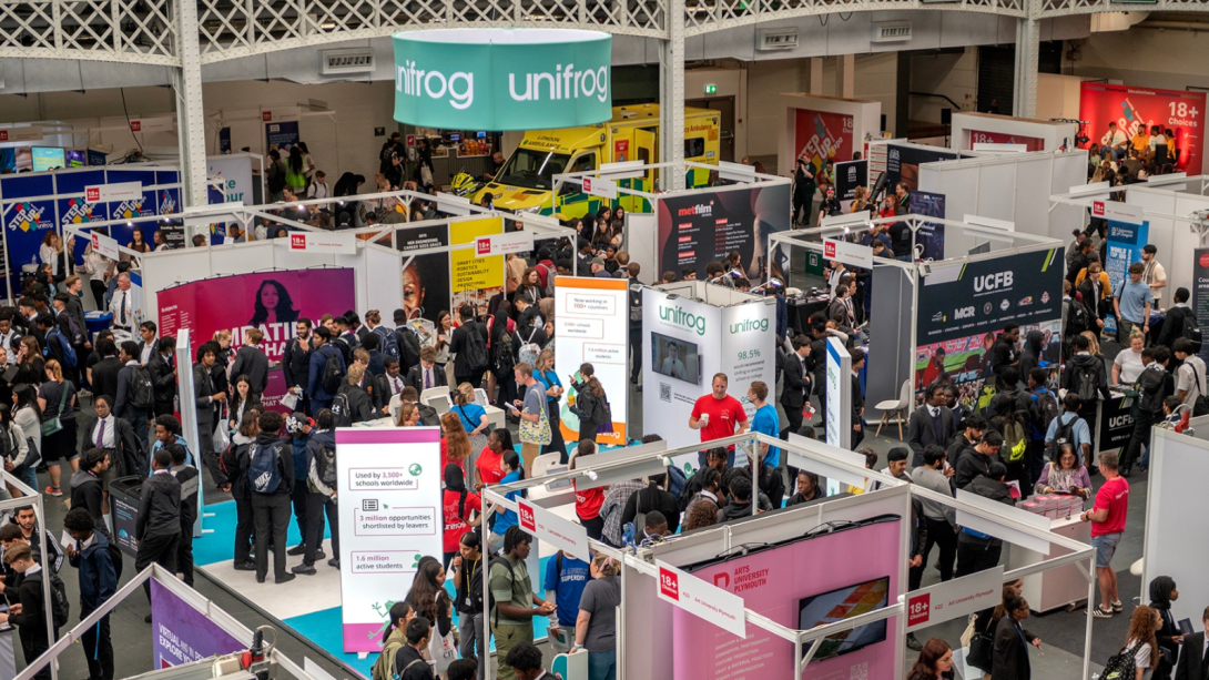 A bustling trade show with a diverse crowd of people gathered together in a large venue.