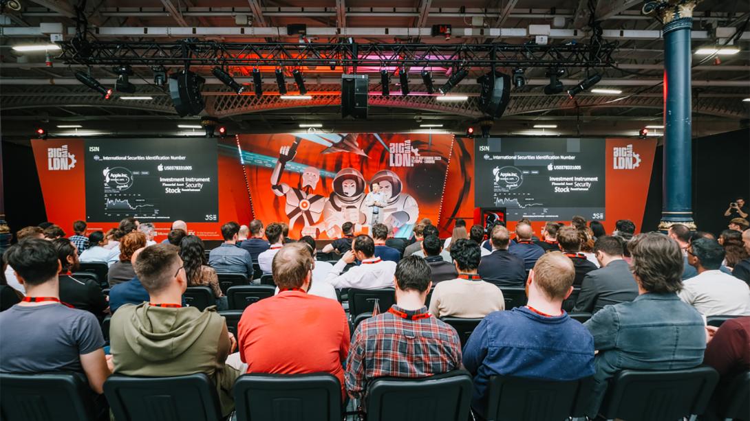 An audience listening attentively to a speaker on stage at a crowded conference.