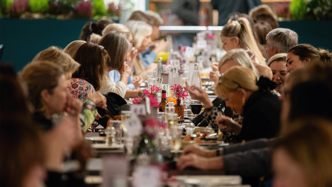 A diverse crowd gathered around a lengthy table, engaged in conversation and sharing a meal together.