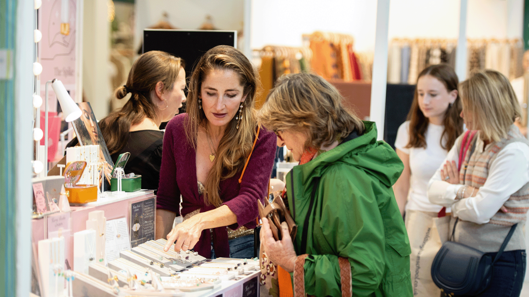 Women browsing handmade crafts at a bustling fair, admiring unique creations and engaging with vendors.