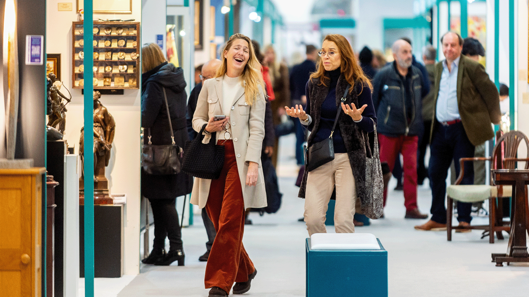 Two women browsing an art show and engaged in conversation.