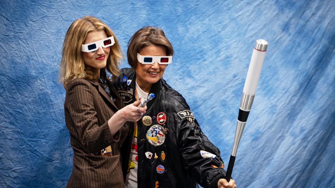 Two smiling women posing together with glasses and props.