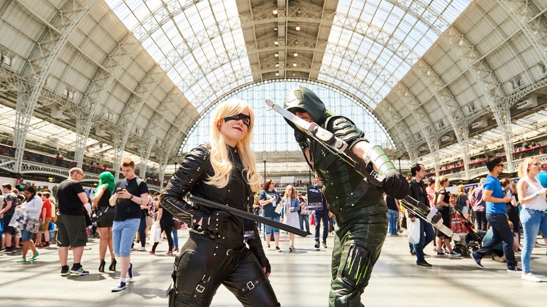 Two individuals dressed as Green Arrow and Arrow, showcasing their costumes with bows and quivers in a dynamic pose.