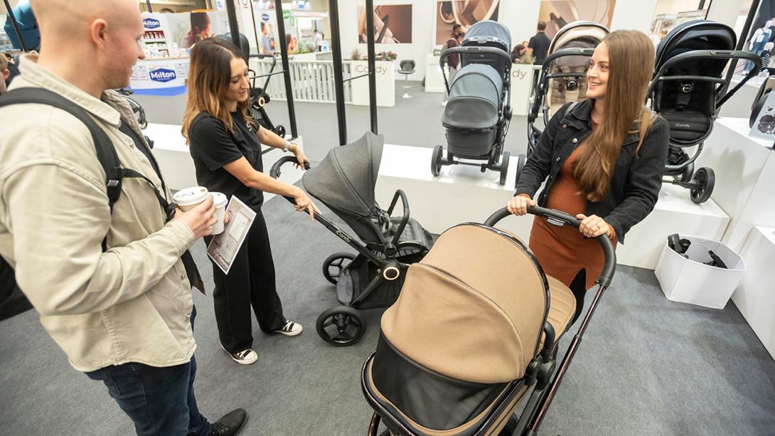 A man and woman observe a stroller, engaged in conversation about its features and suitability for their needs.