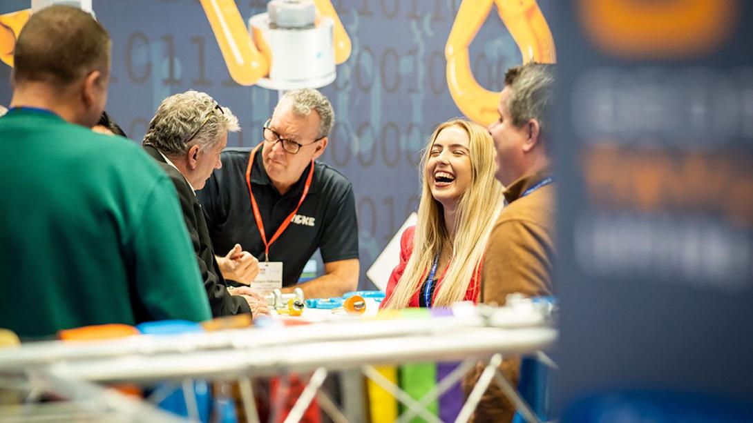 A group of individuals engaged in conversation around a table during a trade event.