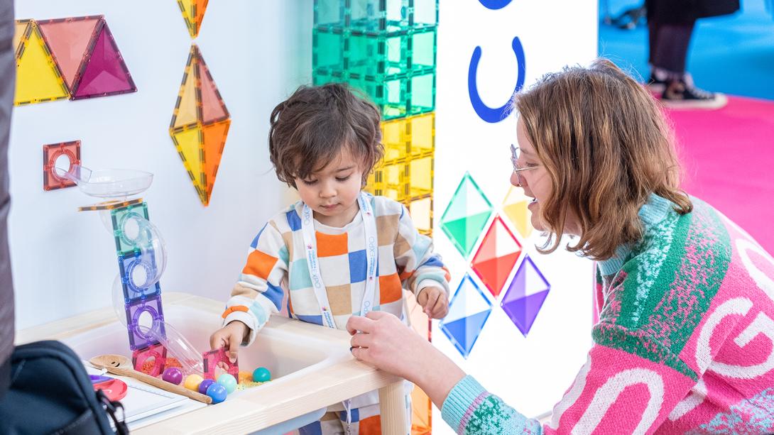 A woman and a child joyfully playing together with vibrant, colorful building blocks on a bright surface.