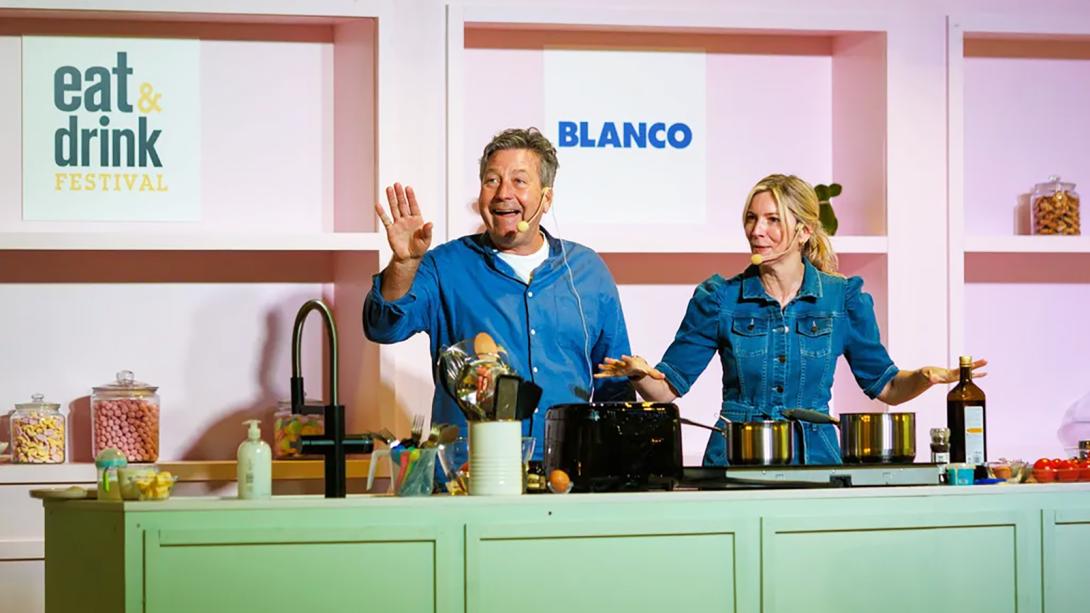 Two individuals stand together in front of a kitchen counter, engaged in conversation or preparing food.