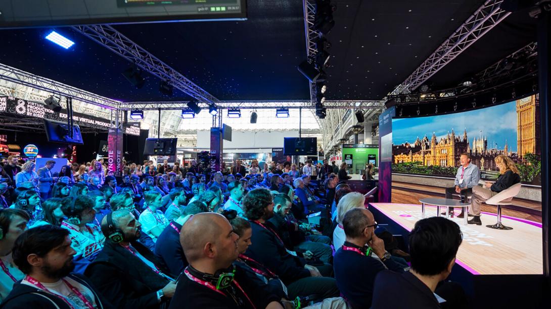 A large crowd attentively watching a presentation displayed on a big screen in a spacious venue.