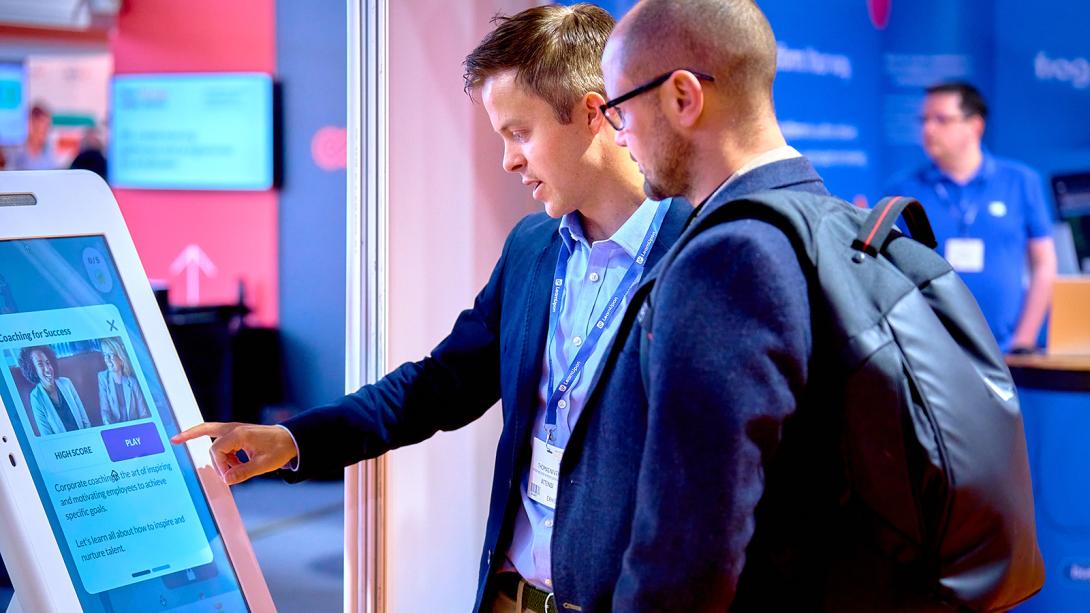 Two men observing a digital display at an event, engaged in discussion and analysis of the information presented.