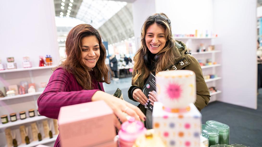 Two women examine a variety of candles displayed on a shelf, showcasing their interest in home decor and ambiance.