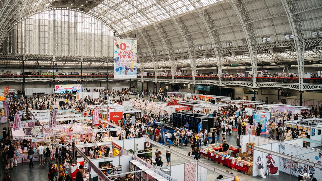 Large indoor event at Hyper Japan Festival 2024 featuring a bustling crowd, colourful stalls, Japanese merchandise, food vendors, and cultural displays.