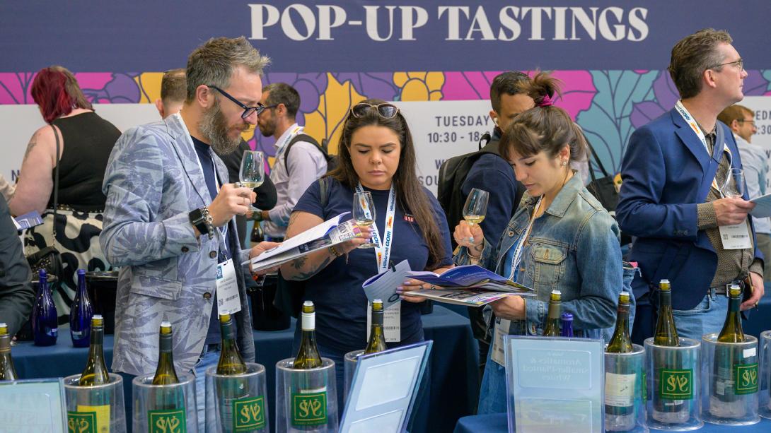 Individuals standing around a table filled with wine bottles.