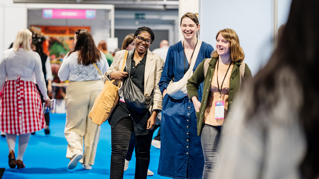  A group of individuals walking together on a vibrant blue carpet at a busy trade event.