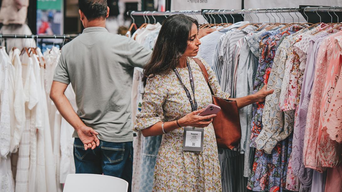 A woman thoughtfully exploring different outfits displayed on the racks.