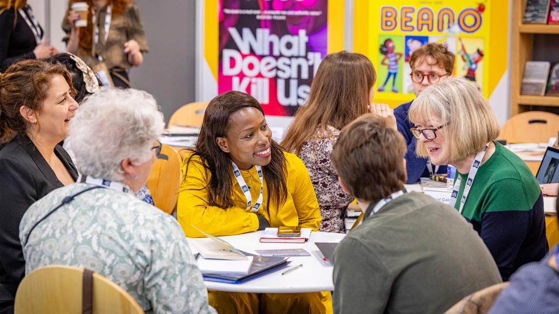 A diverse group of individuals engaged in discussion while seated around a table in a library setting.