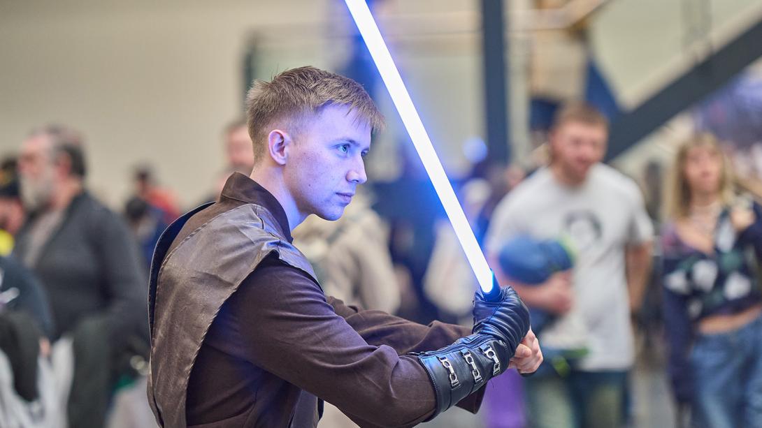 A man in a Star Wars costume stands confidently, wielding a lightsaber in a dynamic pose.