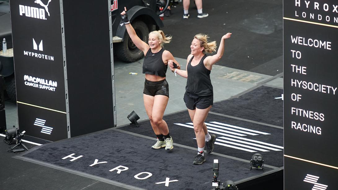 Two women joyfully leap on stage, celebrating their victory at a race, embodying excitement and achievement.