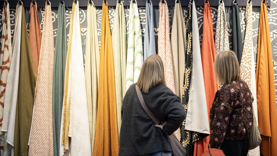 Two women examining colorful fabric samples at a trade show, engaged in conversation and exploring design options.