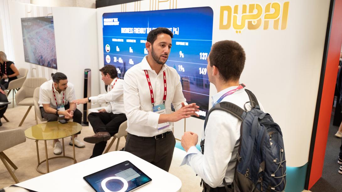 Two individuals are engaged in conversation at a trade show booth.