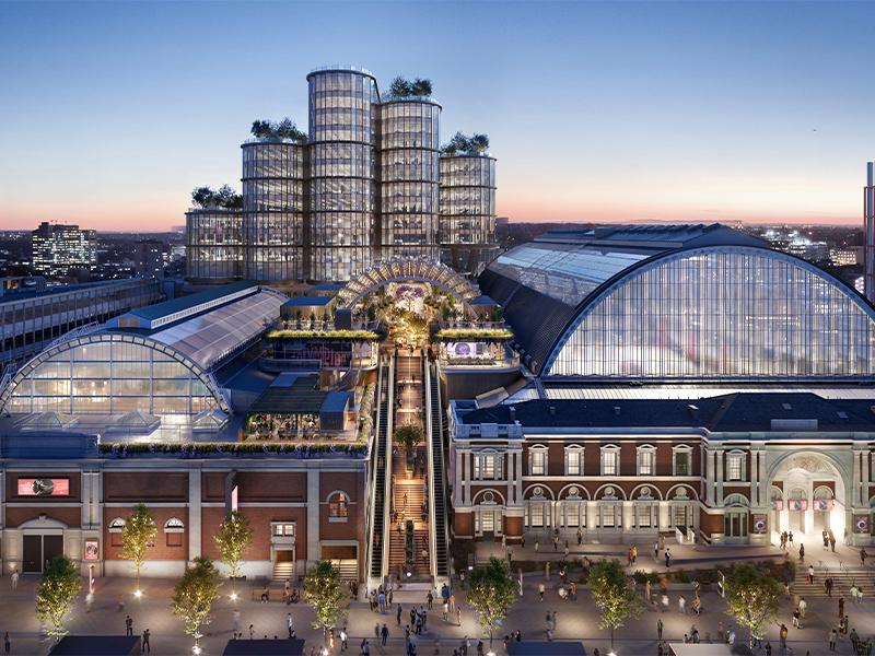 A wide-angle view of the Olympia destination, featuring its iconic arched roofs and new modern glass towers adorned with rooftop greenery.