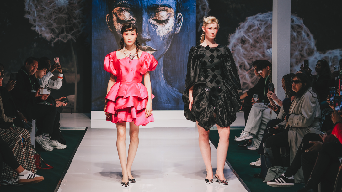 Two people walking down the catwalk in contrasting statement dresses